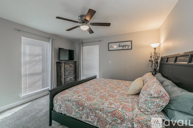 A bedroom with a patterned bedspread and a ceiling fan.