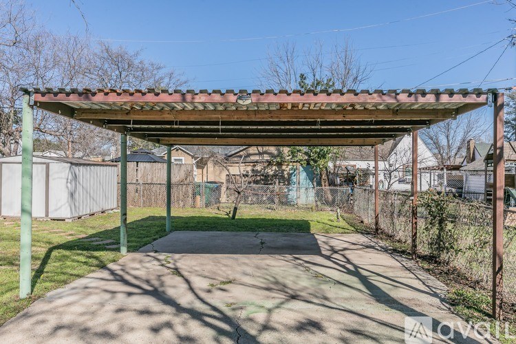 A covered walkway leads to a building with a fence and trees in the background.