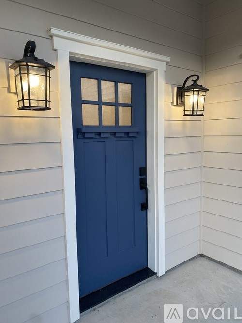 A blue door is flanked by two black lanterns on a white siding wall.