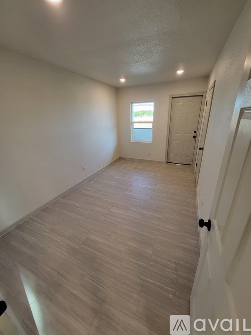 A room with wooden flooring and a door leading to another room.