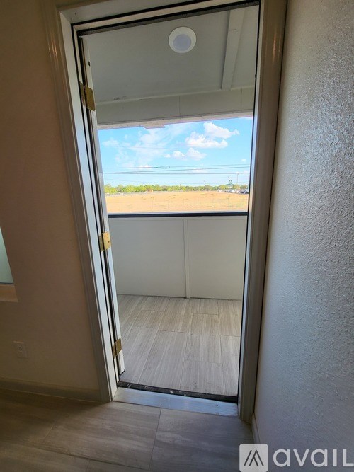 A glass door with a handle is open and leads to a balcony with a view of the sky and a distant landscape.