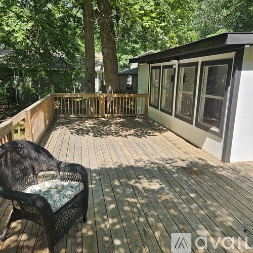 A black wicker chair with a green cushion is on a wooden deck.