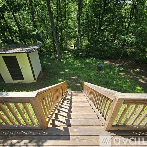 A wooden deck leads to a small cabin in a wooded area.