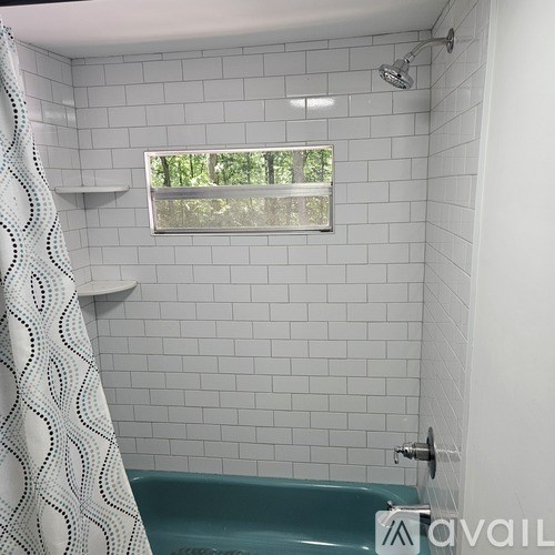 A white tiled bathroom with a green tub and a window.