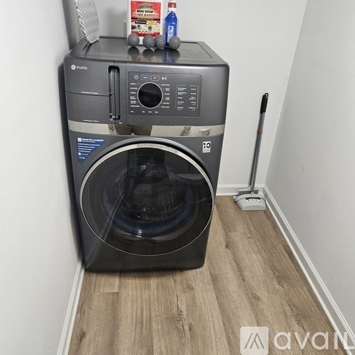 A black front loading washing machine with a bottle of detergent and a box of fabric softener on top.