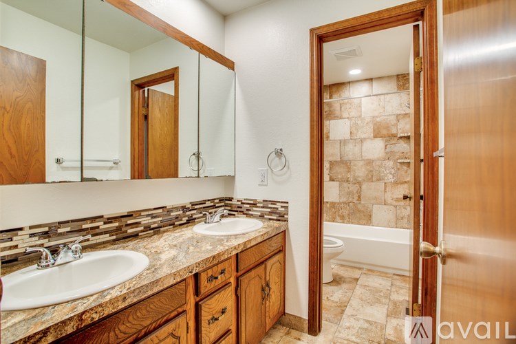 A bathroom with a double sink vanity and a tub in the background.
