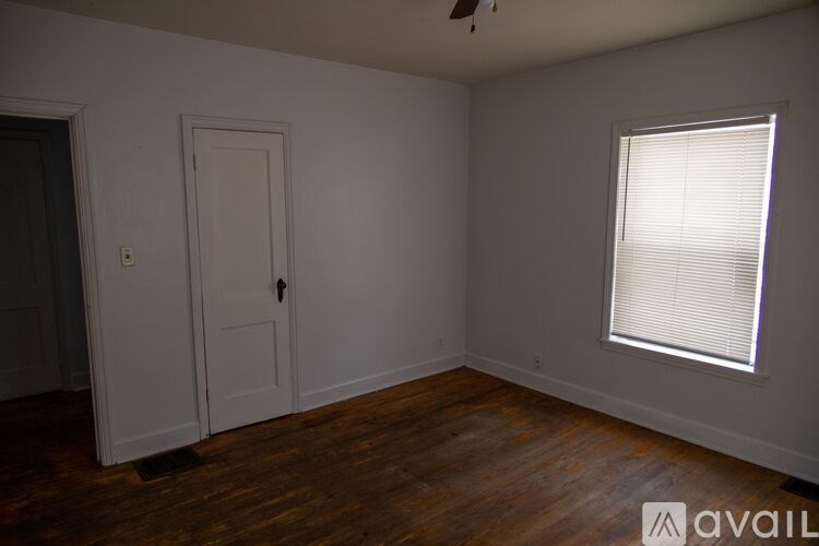 A room with a wooden floor, a door, and a window with blinds.