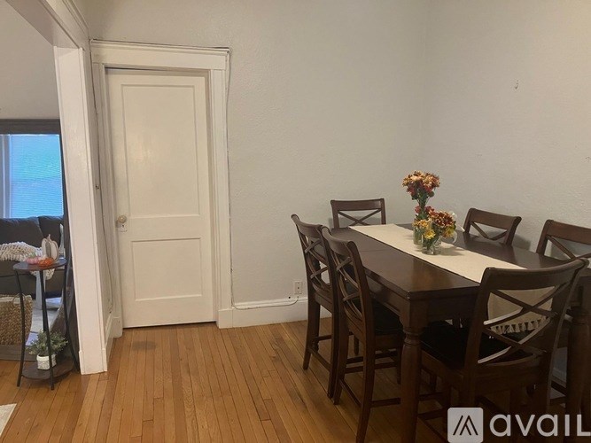 A dining room with a white door, a table with chairs and a vase of flowers.