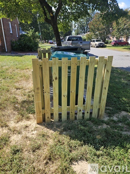 A wooden fence in front of a grassy area with a car and houses in the background.