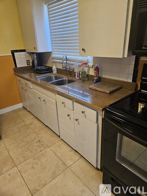 A kitchen with a sink, a window with blinds, and a black oven.