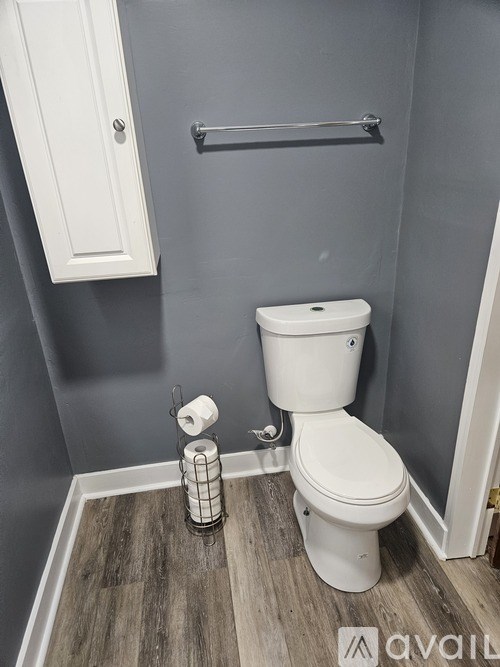 A white toilet with a roll of toilet paper on the floor.