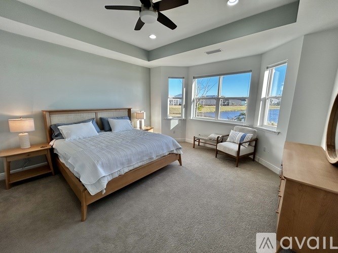 A bedroom with a large bed, a ceiling fan, and a view of the outdoors through the windows.