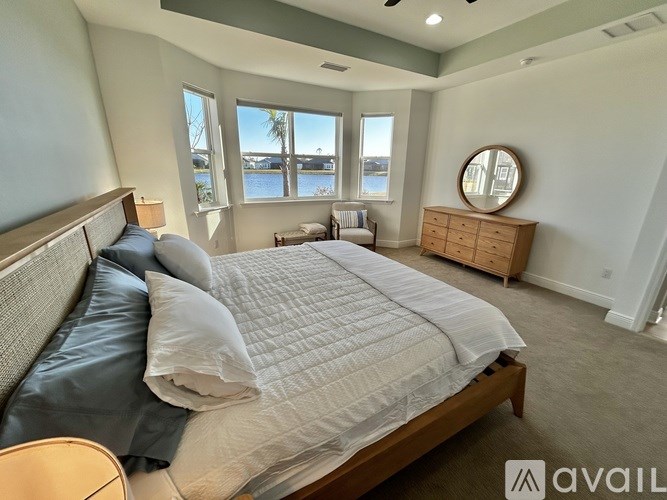 A bedroom with a large bed and a view of the water through the windows.