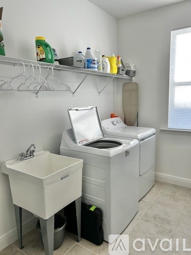 A laundry room with a washer and dryer, sink, and shelves with cleaning supplies.