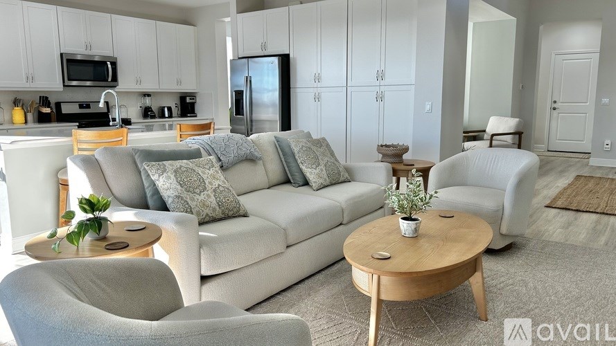 A modern living room with a grey sofa, wooden coffee table, and a kitchen area in the background.