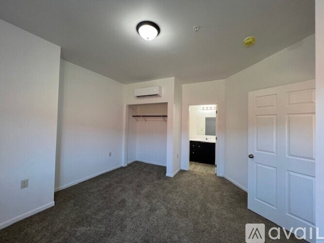 A room with a carpeted floor, a ceiling light, and a wall-mounted air conditioner unit.