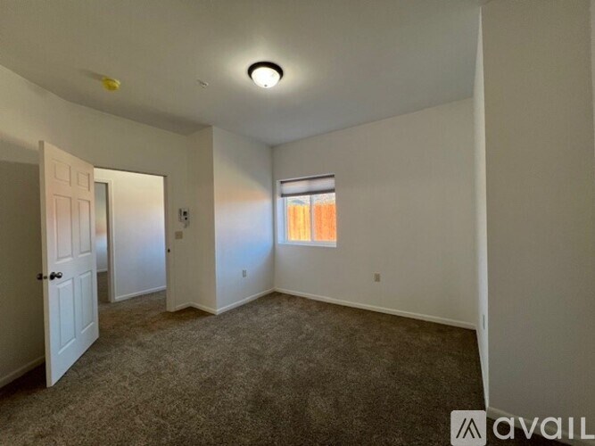 A room with a carpeted floor and a window with orange curtains.