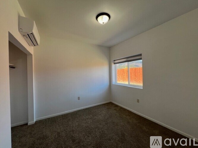A room with a carpeted floor, a window with orange curtains, and a ceiling fan with a light fixture.