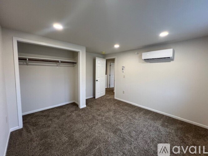 A spacious room with a carpeted floor, a closet with a shelf, and a wall-mounted air conditioner unit.