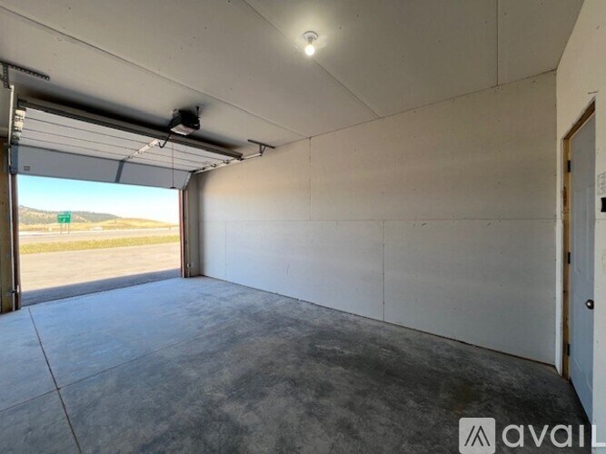 A large empty room with a garage door open to a parking lot.