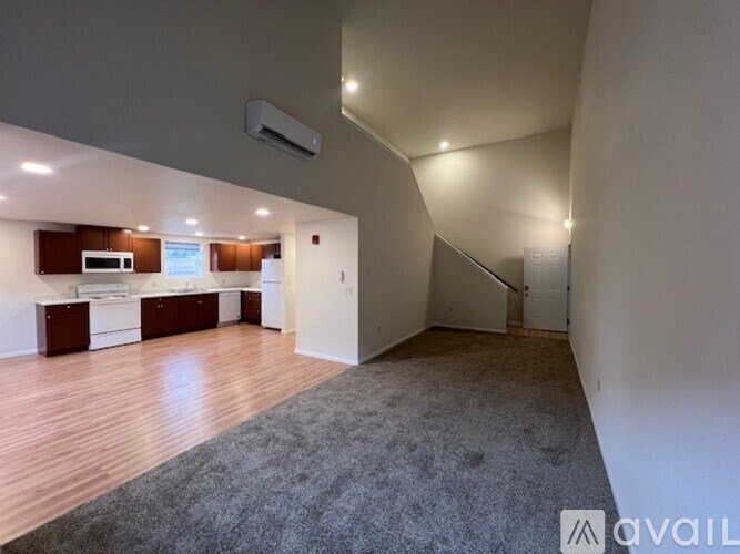 A spacious room with wooden flooring and a kitchen area in the background.