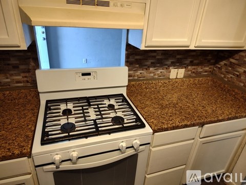 A white gas stove with four burners is in a kitchen with granite countertops.