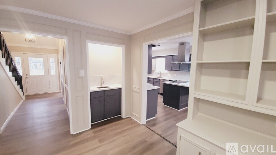 A spacious room with wooden floors and white walls, featuring a staircase on the left and a kitchen area on the right.