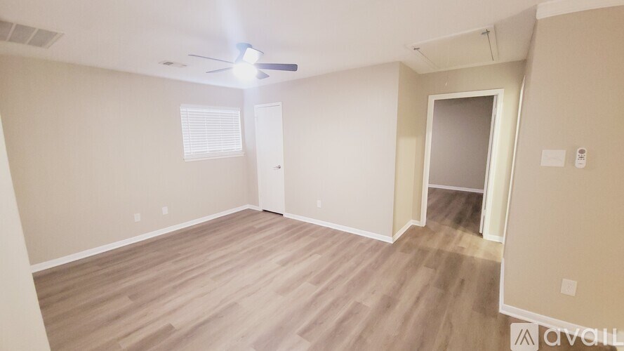 A spacious room with a ceiling fan and light, hardwood flooring, and a doorway leading to another room.