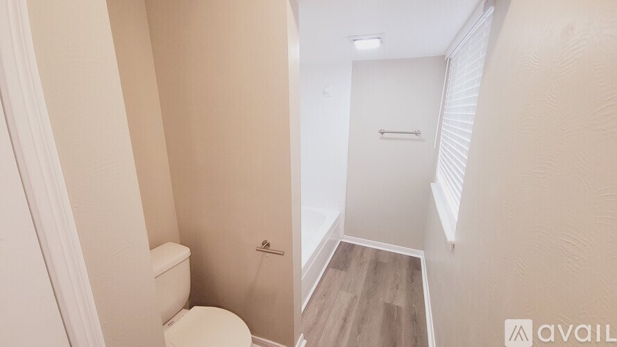 A bathroom with a toilet and a wooden floor leading to a hallway.