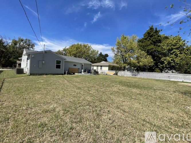 A house with a grey roof is surrounded by a fence and a grassy field.