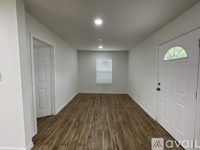 A room with wooden flooring and white walls, with a window covered by white blinds.