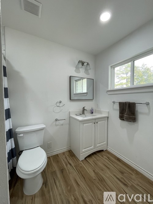 A small white bathroom with wood flooring and a window.