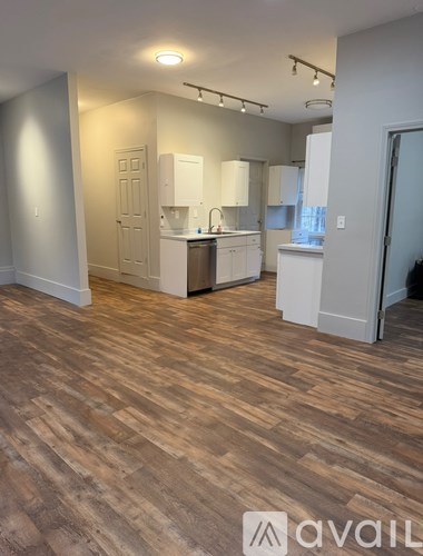A room with wooden flooring and a kitchen area with white cabinets.