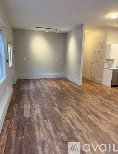 A room with wooden flooring and a kitchen area in the background.