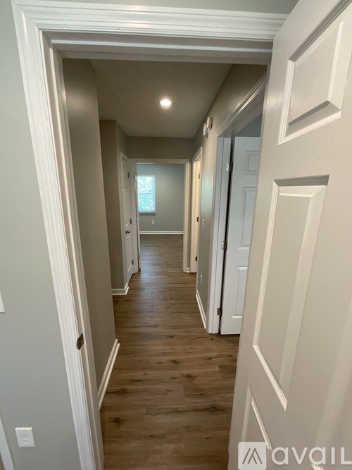 A hallway with white walls and wood flooring.