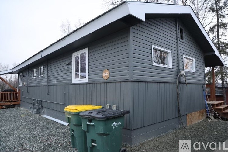 A grey house with a yellow trash bin in front.