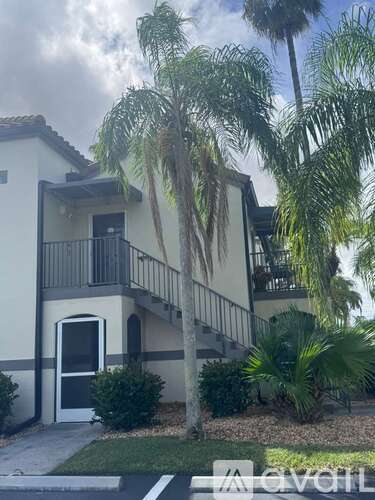 A building with a balcony and a door is surrounded by palm trees.