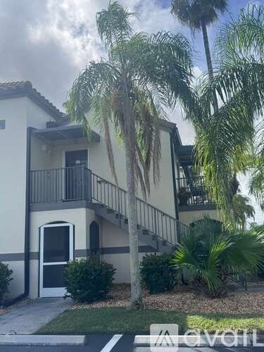 A building with a balcony and a door is surrounded by palm trees.