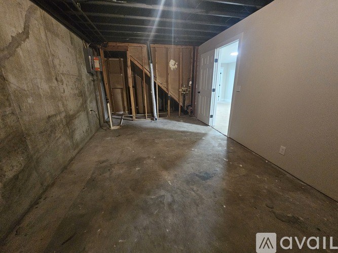 A room with a concrete floor and walls, and a wooden staircase in the background.