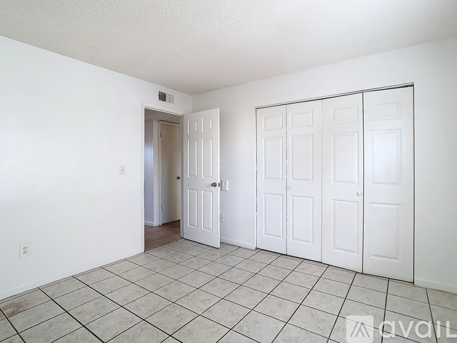 A room with white walls and a tiled floor with a door on the left and three closets on the right.