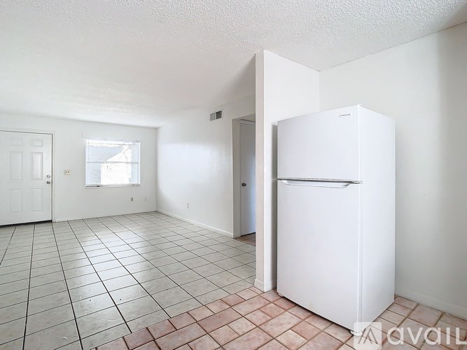 A white refrigerator is in a kitchen with tile flooring and white walls.
