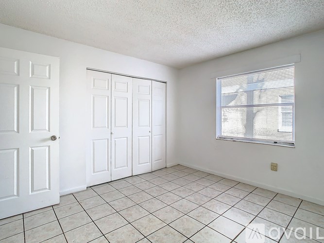 A room with white walls, a white door, a window with blinds, and a tiled floor.