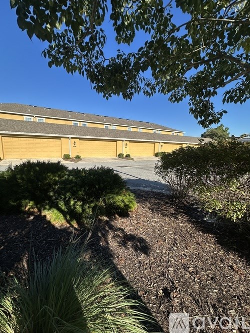 A building with a yellow garage door is surrounded by trees and shrubs.