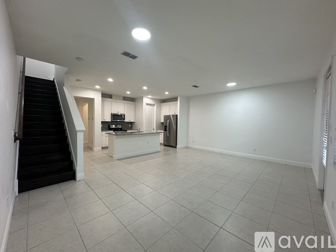 A spacious, empty room with a staircase on the left and a kitchenette in the background.