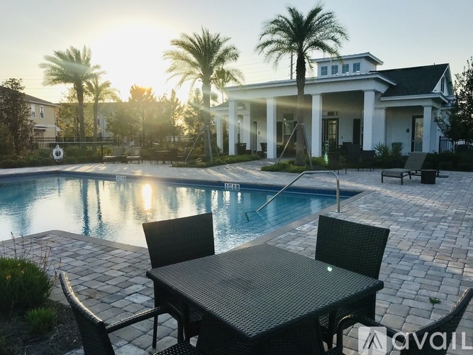 A poolside table and chairs are set up in front of a house with a pool.