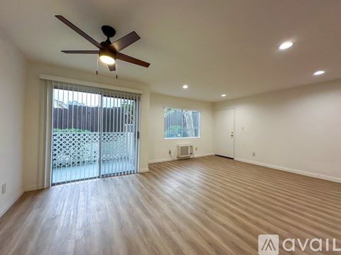 A spacious room with a ceiling fan and sliding glass doors leading to a balcony.