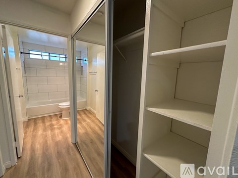 A white walk-in closet with shelves and a bathroom visible through the glass door.