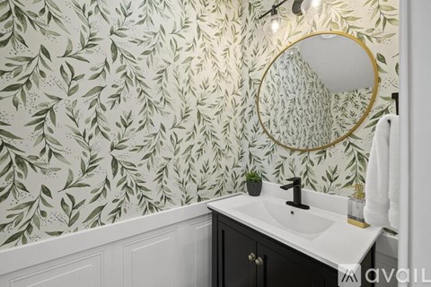 A bathroom with a leaf patterned wallpaper and a round mirror.