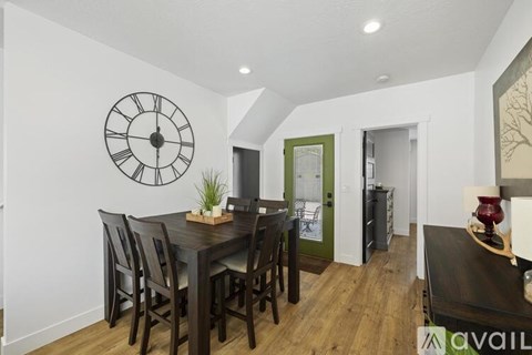 A dining room with a wooden table and chairs, a clock on the wall, and a green door in the background.
