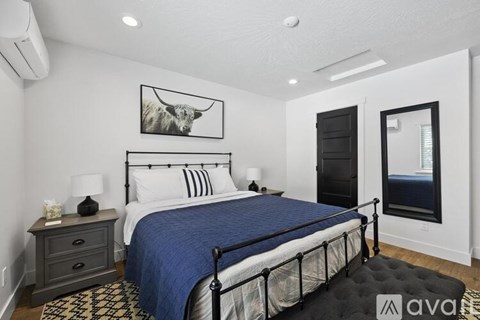 A bedroom with a large bed, a nightstand with a lamp, and a framed picture of a cow on the wall.